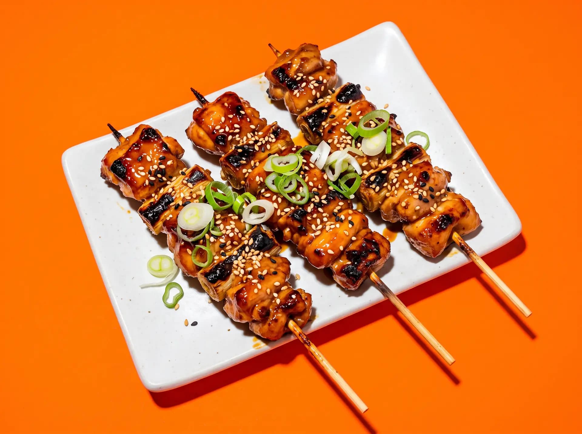 Brochettes yakitori laquées au sésame et oignon nouveau sur fond orange vif